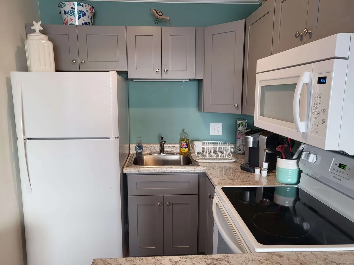 This image showcases a modern kitchen featuring gray cabinets, stainless steel appliances, a sleek granite countertop, and a deep sink. The space is designed to be both functional and stylish, inviting guests to cook, bake, and socialize in a welcoming atmosphere.