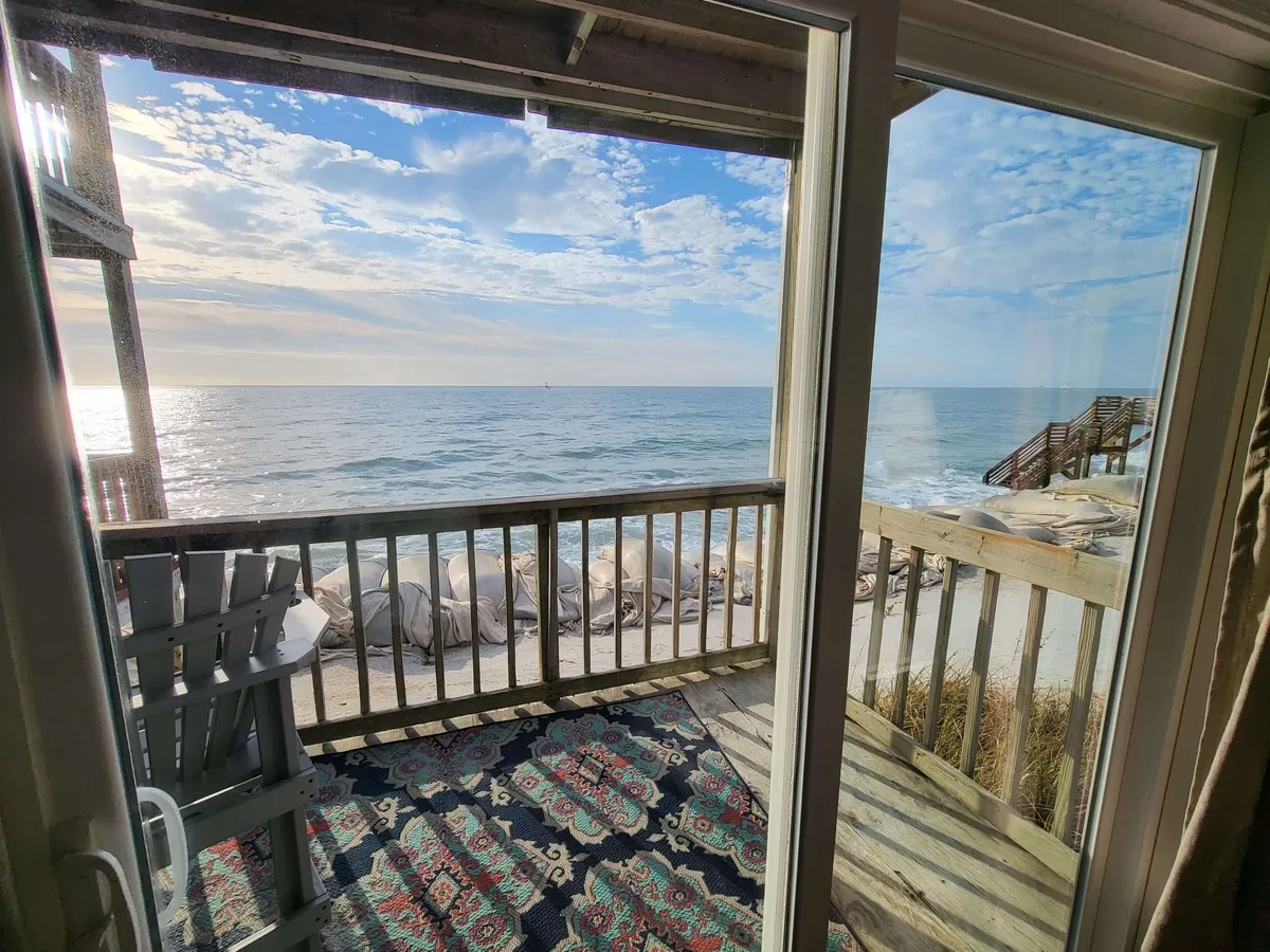A peaceful balcony scene featuring comfortable patio furniture and a wooden railing, all oriented to maximize sweeping ocean views. The area rug and casual setup invite relaxation, whether for morning coffee or sunset cocktails.