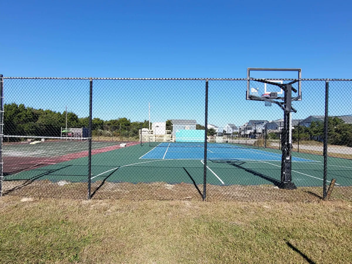 This exterior image features a basketball hoop, tennis courts, a fence, and green grass, suggesting ample space for outdoor recreation. The scene is lively and active, underscoring opportunities for engaging in sports or gathering with others outdoors.