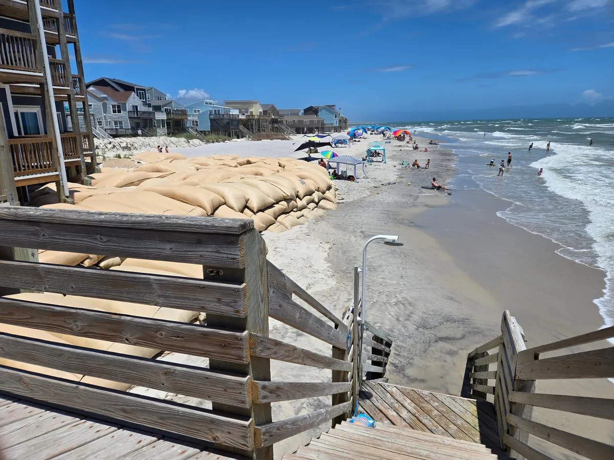 This image captures people enjoying a lively day at the beach, with umbrellas providing shade, children playing in the sand and water, and gentle waves in the background. The casual, welcoming atmosphere reflects a typical family-friendly beach outing.