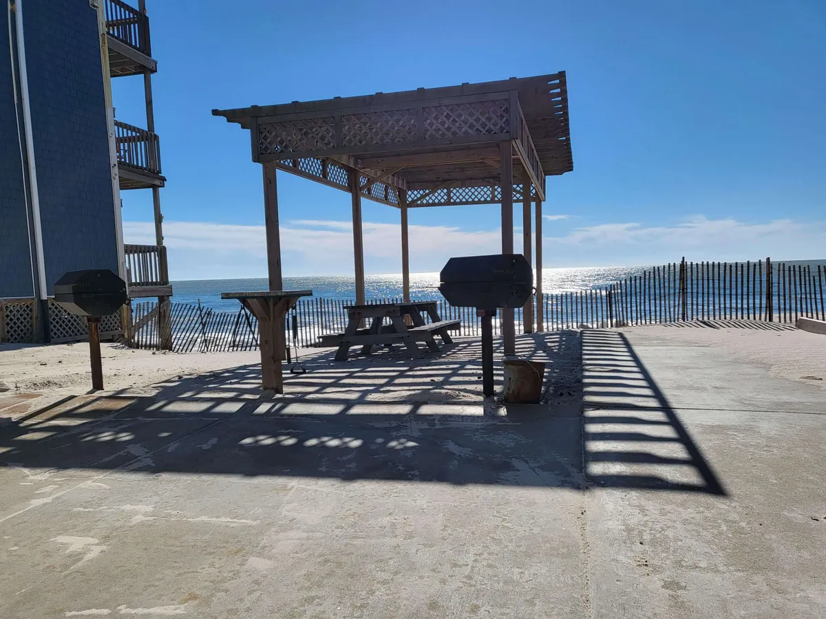 An inviting oceanfront picnic area with a wooden gazebo, picnic table, grills, and panoramic ocean views, ideal for gatherings, meals, and outdoor fun.