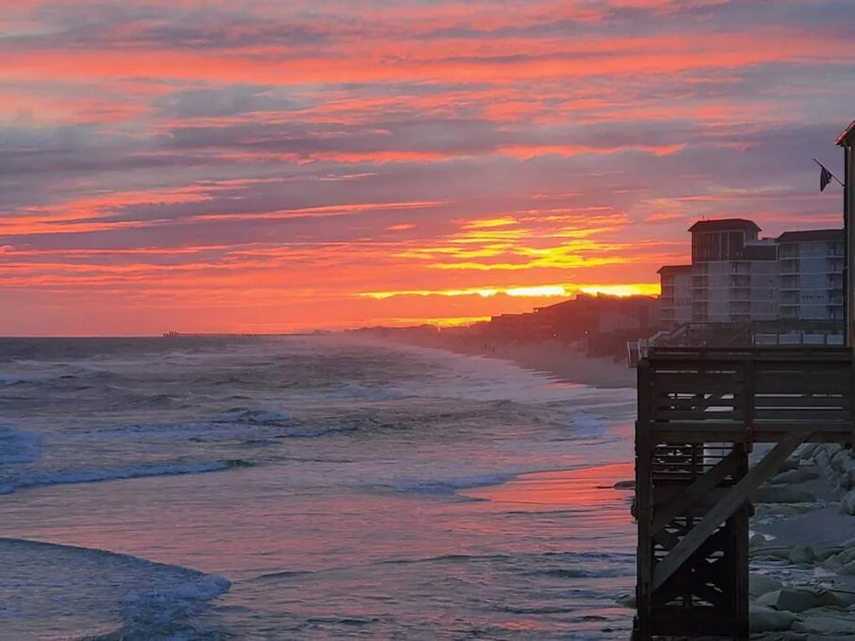 This image captures a breathtaking sunset over the ocean, with gentle waves, a pier extending into the water, and beachfront buildings, all bathed in serene twilight. The scene radiates romance and tranquility, evoking the ideal setting for couples seeking memorable moments by the sea.