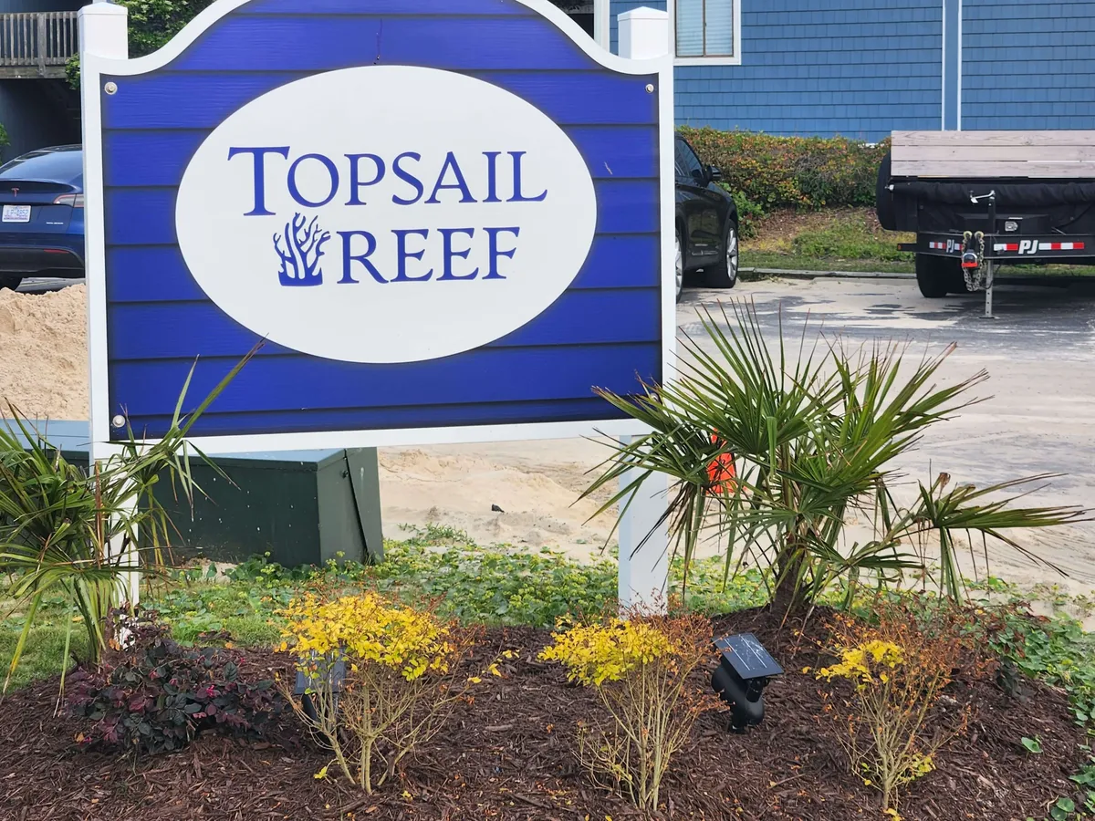 This image shows the Topsail Reef sign surrounded by colorful plantings and lush greenery, setting a welcoming scene at the property entrance. The view highlights the inviting atmosphere and the vibrant, coastal environment that guests first experience upon arrival.
