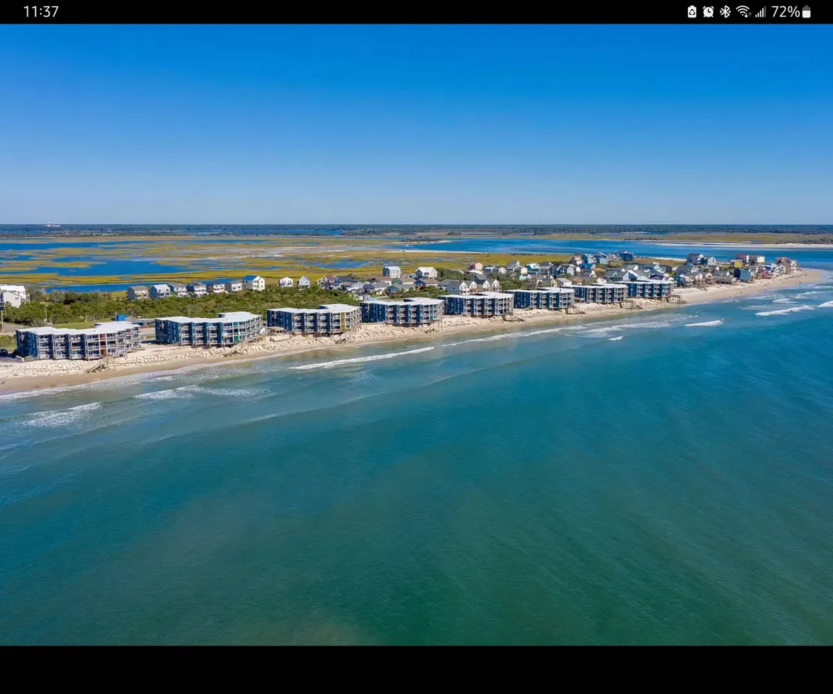 This image captures the exterior view of oceanfront properties set against a backdrop of the sea and distant marshlands. The relaxed mood is established by early morning or late afternoon light, gentle waves, and the natural expanse surrounding the condo—a scene that promises tranquility and connection with the elements.