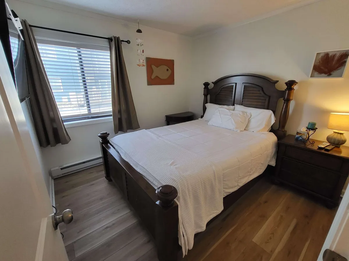A tranquil bedroom featuring a wooden bed frame with soft bedding, a nightstand with a lamp, and fish-themed wall art. The gentle lighting and muted tones create an atmosphere of peaceful relaxation.