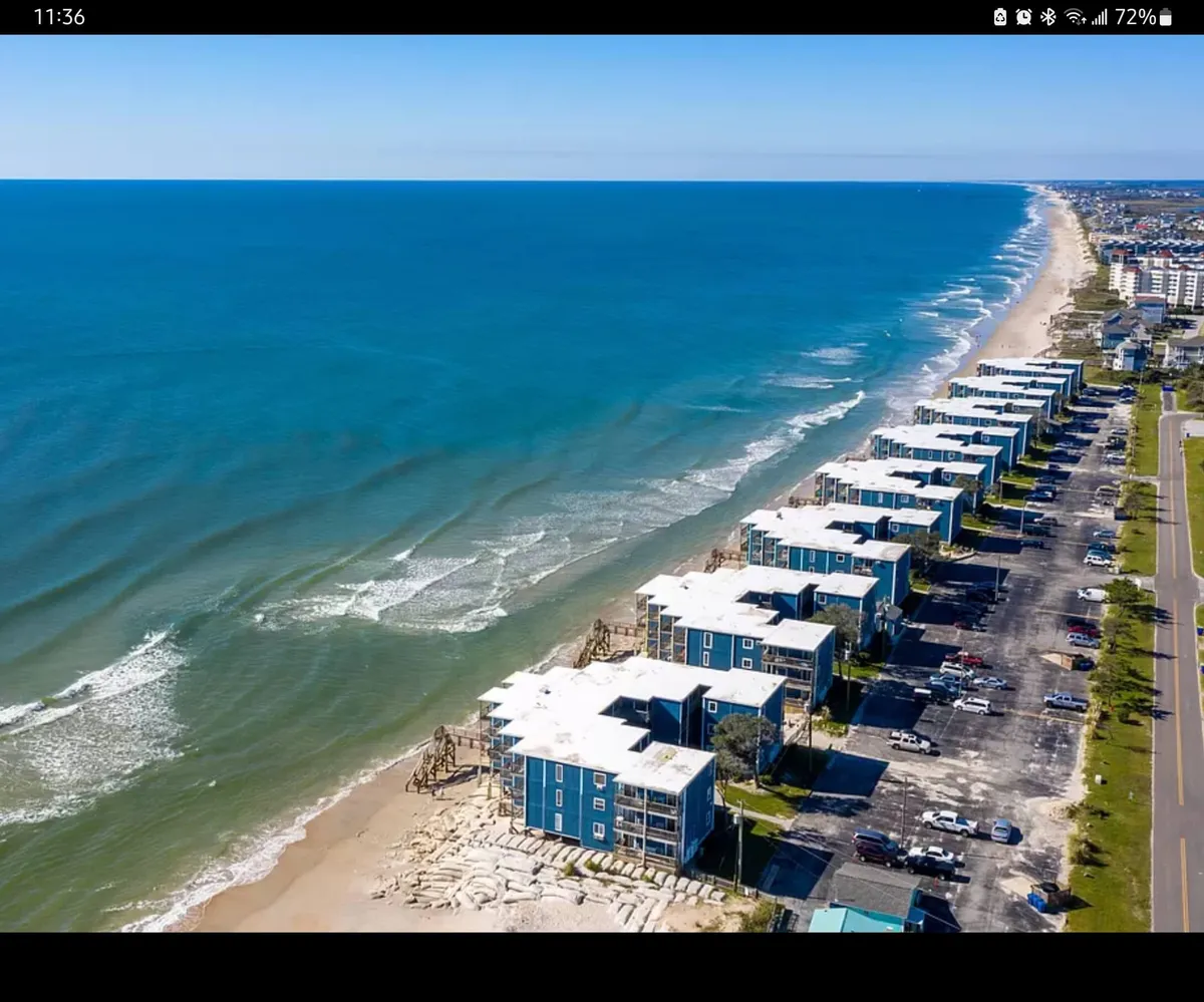 A serene view of beachfront properties bordering the ocean, with rolling waves and a spacious parking area in the foreground. The image exudes tranquility and the promise of quick access from your door to the water's edge.